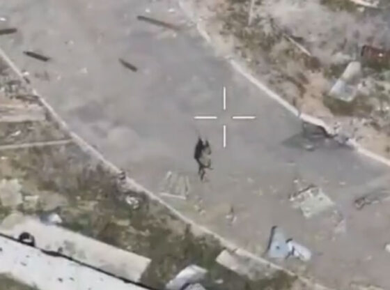 A crosshair targeting a person on a street in a war-torn settlement.