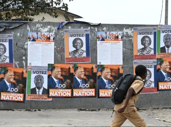 A middle school student walks past campaign posters of Ivorian President and presidential candidate for the Rally of Houphouetists for Democracy and Peace (RHDP), Alassane Ouattara, and former Ivorian First Lady and presidential candidate for the Movement of the Capable Generation (MGC), Simone Ehivet Gbagbo, in the commune of Treichville in Abidjan on October 14, 2025. (Photo by Sia KAMBOU / AFP)