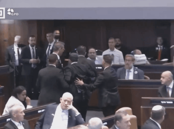 People in formal attire engaged in a heated discussion in a large room.