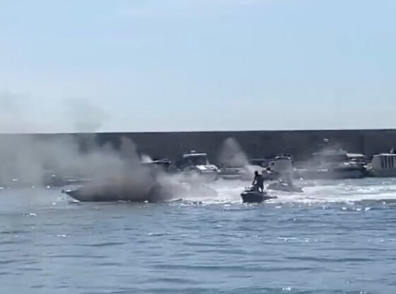 A jet ski helps firefighters put out a fire on a boat, creating a large plume of smoke.