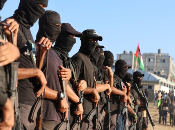 Palestinian militants in balaclavas and black caps stand guard with automatic rifles.