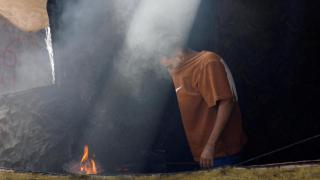 A Palestinian man cooks food over a fire in his tent, in Nuseirat.