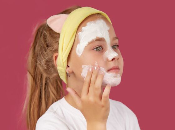 A little girl puts on a cosmetic mask on an isolated red background. by Юрий Дровнин ادوبي ستوك