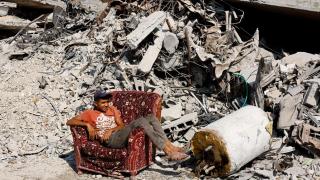 A young Palestinian sits in an armchair among the ruins of Gaza City.